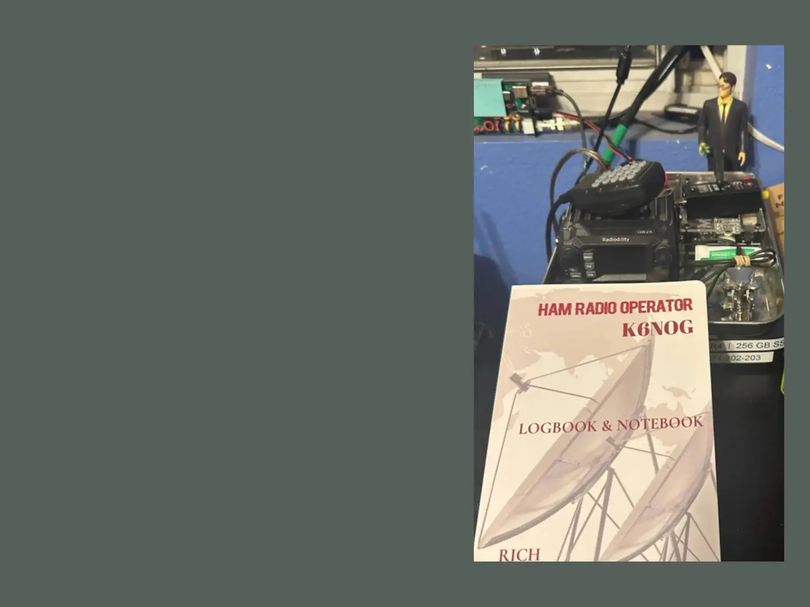 A Ham Radio Operator  logbook and notebook cover is displayed in the foreground on a desk, with walkie-talkies and electronic equipment in the background against a blue wall.