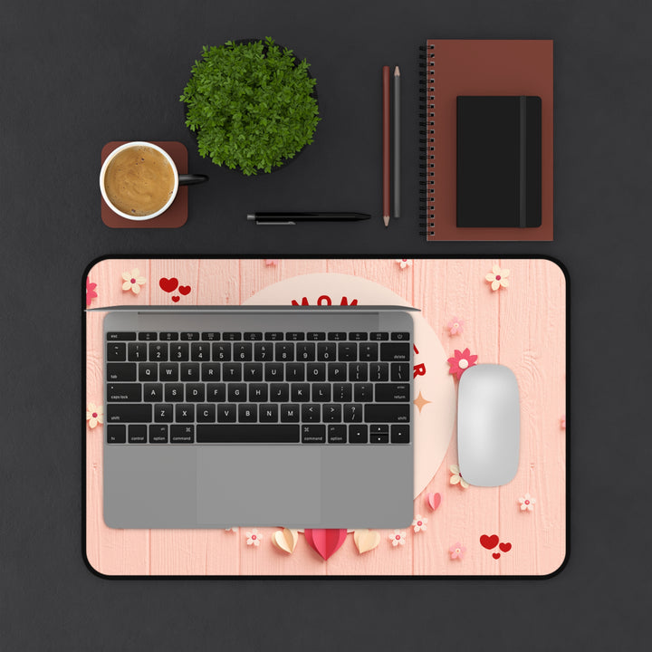 Laptop on a decorative mouse pad with a cup, plant, and stationery items on a dark surface