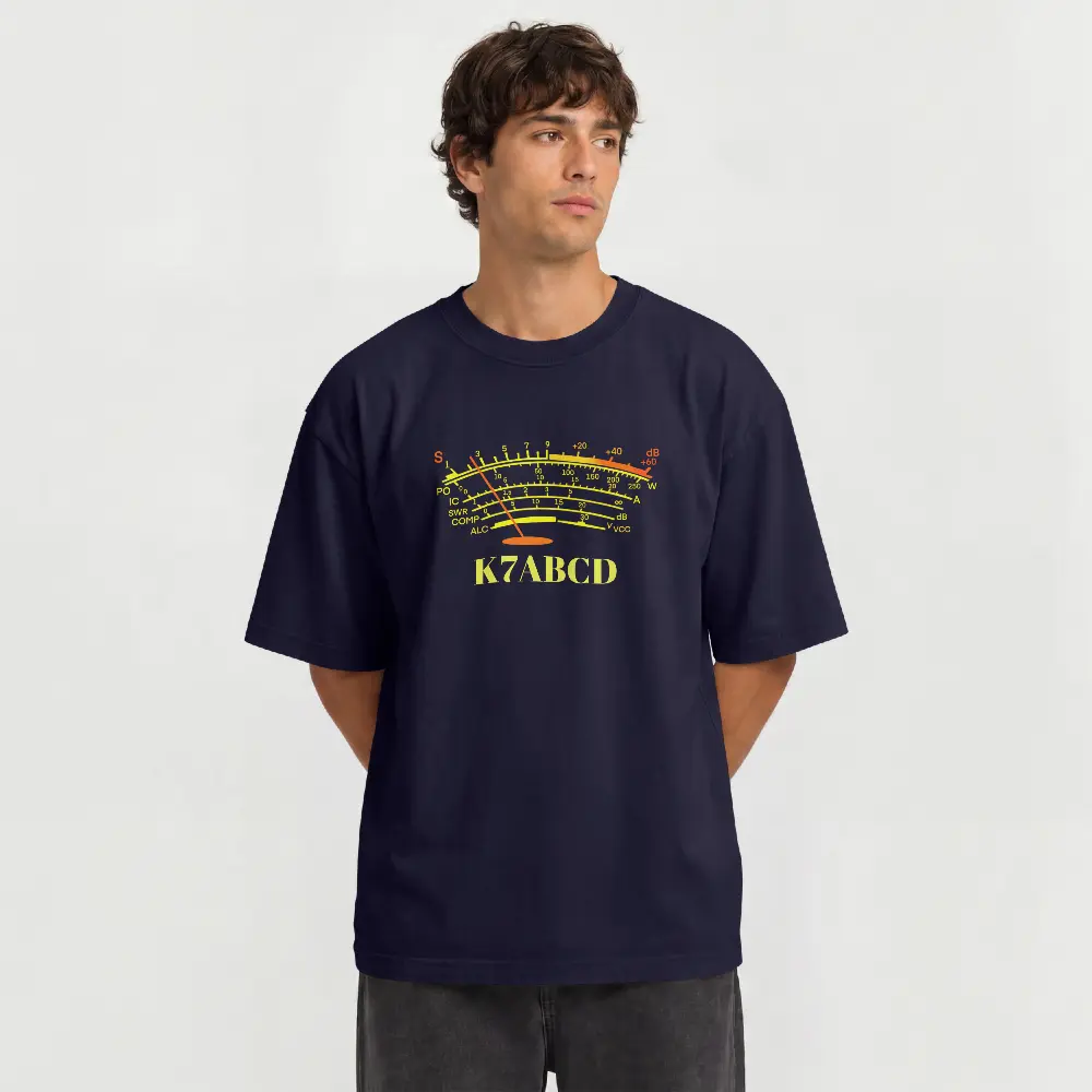 A man wearing a navy blue t-shirt with a yellow and red analog S meter graphic and the text 'K7ABCD' printed on the chest, set against a plain light gray background.