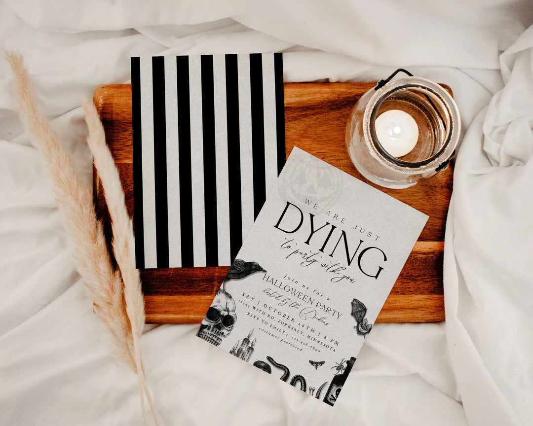 Halloween party invitation with black and white design on a wooden tray with a candle.