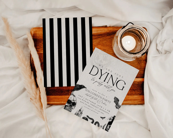 Halloween party invitation with black and white design on a wooden tray with a candle.